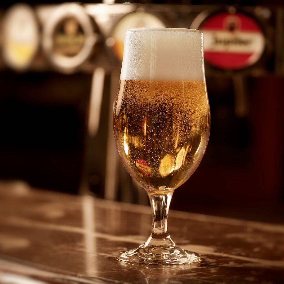 Gevuld bierglas op voet Munich 49 cl. met goudkleurigbier en witte schuimkraag op bar